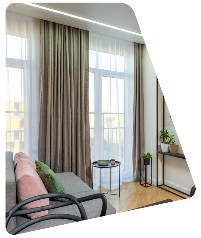 Modern living room with a gray sofa, green cushions, and large windows with curtains.