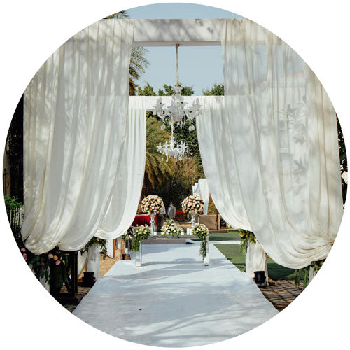 Decorative outdoor setting with white curtains, chandelier, and floral arrangements.
